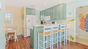 Une cuisine avec des meubles de couleur turquoise, un réfrigérateur blanc et un coin bar avec des tabourets.