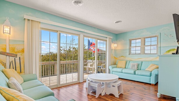 Un salon spacieux doté d’une grande porte-fenêtre coulissante donnant sur un balcon, d’un canapé bleu clair, d’une table basse blanche et d’un divan de couleur turquoise.