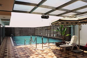 Une piscine intérieure dotée d’un sol carrelé, d’un plafond en verre et d’un espace au bord de la piscine comprenant une chaise et un pot de fleurs.