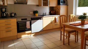Une cuisine moderne avec des meubles en bois, un four encastré, un four à micro-ondes et un coin repas comprenant une table et des chaises.