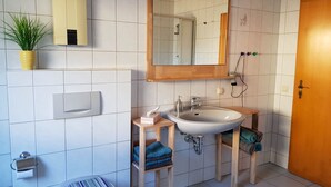 Une salle de bain avec un lavabo blanc, un meuble-lavabo en bois, un miroir, un porte-serviettes, des toilettes et une plante en pot.