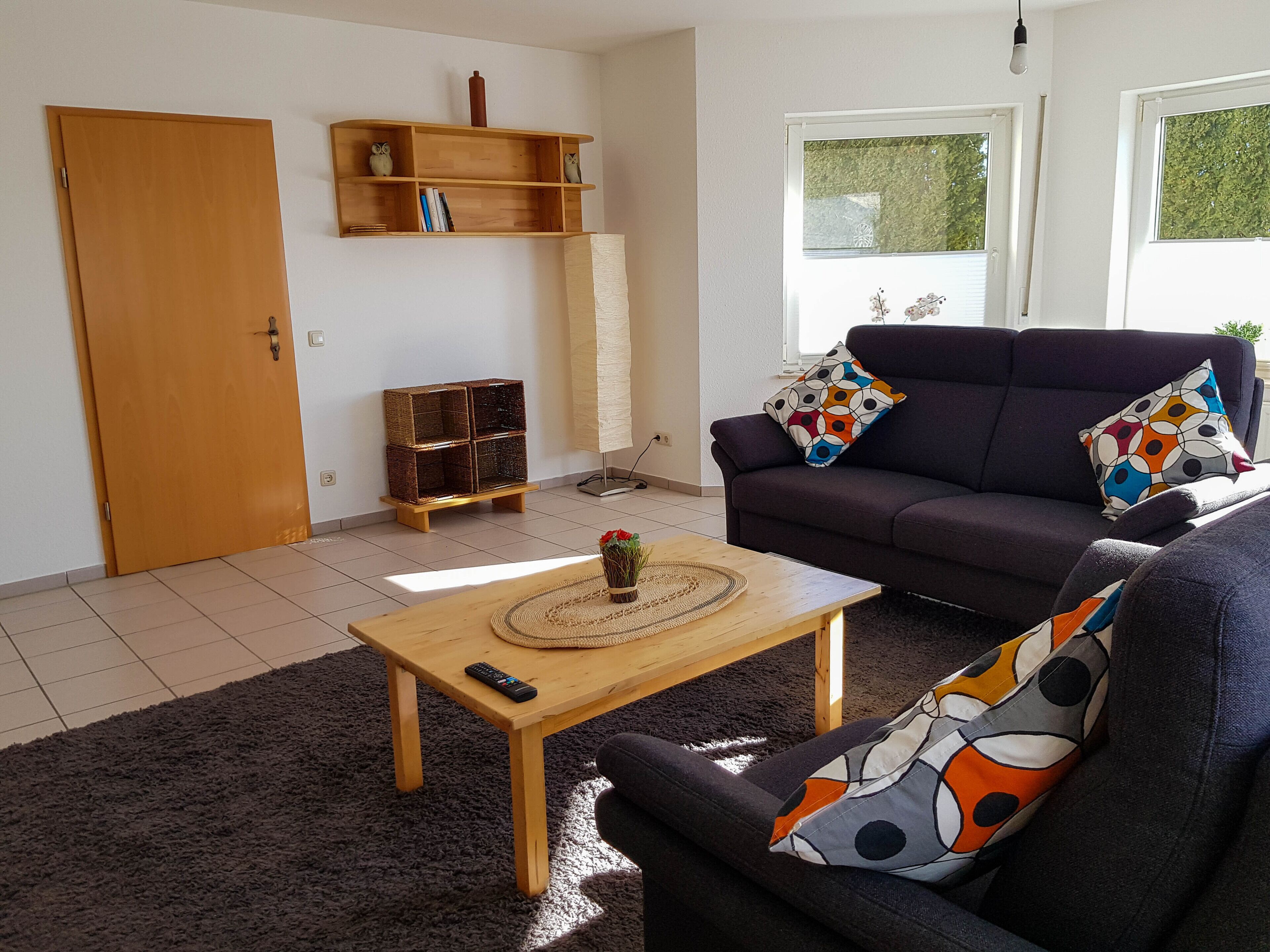 Een woonkamer met een bank, een bijzettafeltje, een boekenkast en een deur.