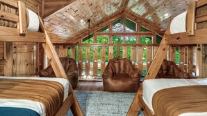 Une cabane en bois avec deux lits, un lit en mezzanine et une grande fenêtre donnant sur un paysage verdoyant.