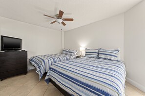 A bedroom with two beds, a ceiling fan, a TV on a dresser, and a bedside lamp.