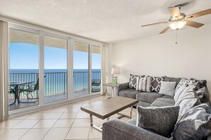 A balcony with a view of the ocean, a ceiling fan, and a sofa with patterned cushions.