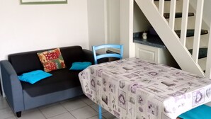 A room with a sofa, a table with a patterned tablecloth, a staircase, and a framed picture on the wall. - Vacation home 200 m from the beach (VALRAS PLAGE)