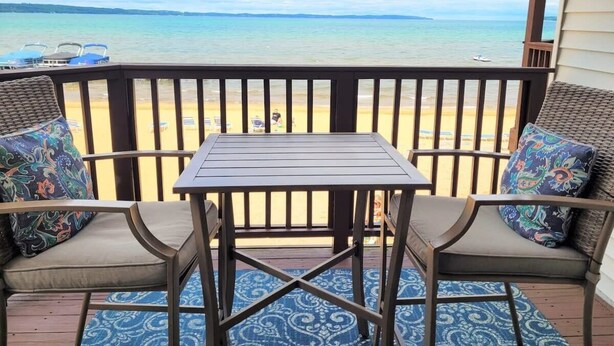 A balcony with a table and two chairs, overlooking a beach.