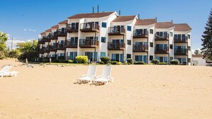 A beachfront hotel with multiple balconies, a sandy beach in the foreground, and a clear blue sky.