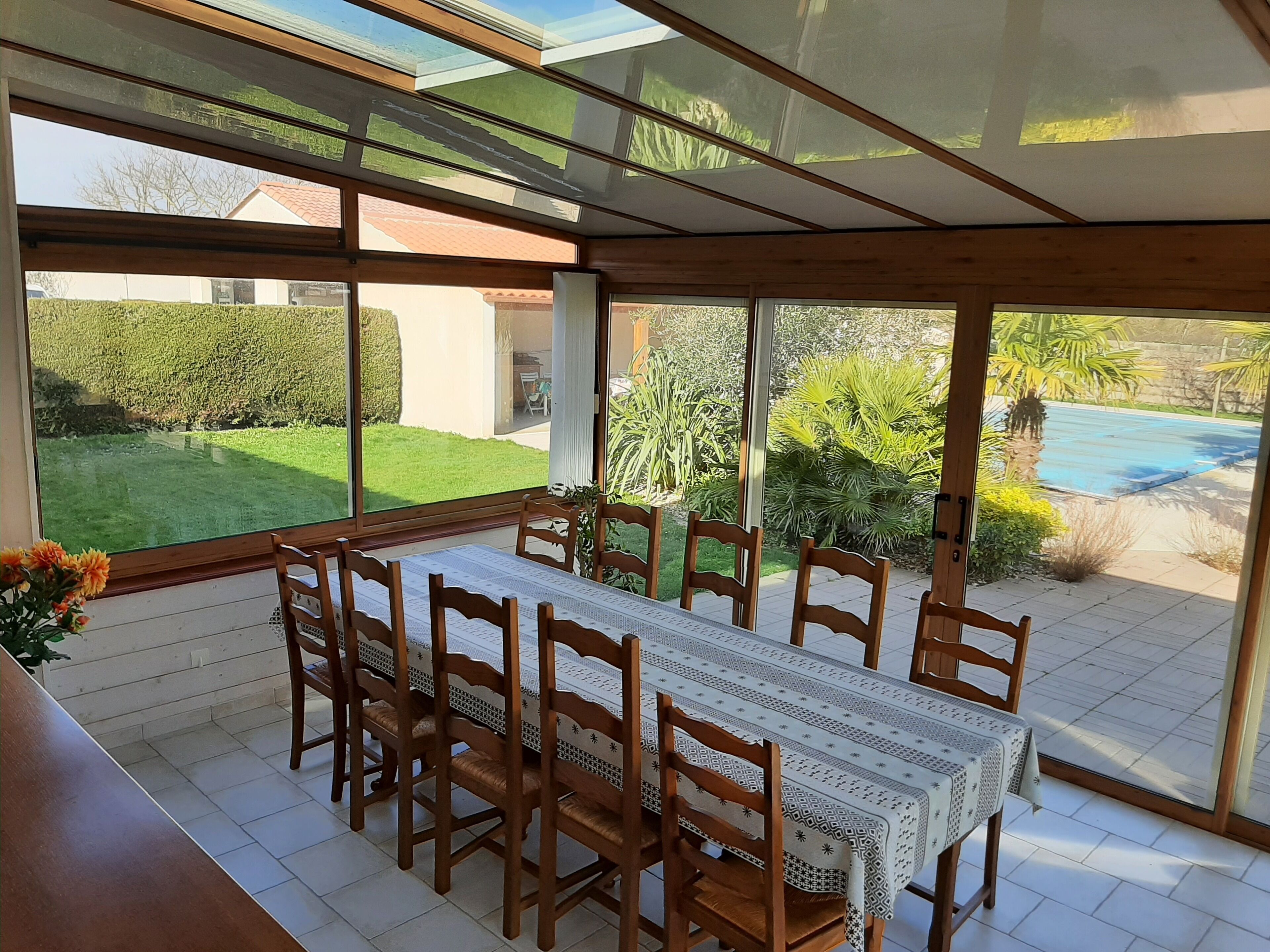 Un espace repas comprenant une table et des chaises, de grandes fenêtres et une vue sur un jardin et une piscine.