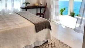 Een slaapkamer met een bed, een plafondventilator, uitzicht op zee en een balkon.