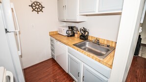 Een compacte keuken met witte kasten, een houten aanrecht, een roestvrijstalen spoelbak en een koffiezetapparaat.