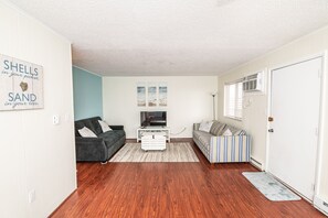Een woonkamer met een donkergrijze bank, een gestreepte bank, een witte tv-meubel en een houten vloer.