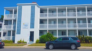 Een meerlaags hotel met balkons, een bord met 'Summer Winds' op de begane grond, en een geparkeerde SUV ervoor.