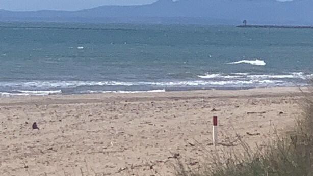 Une plage avec un drapeau signalant la limite du rivage, une chaîne de montagnes lointaine et un ciel dégagé.