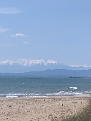 A beach with a flag marking the shoreline, a distant mountain range, and a clear sky.