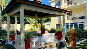 A covered outdoor seating area with a stone fountain, potted plants, and a decorative shell sculpture. - Family Friendly~Chef Service- Book 8 to 14 Rooms (Sosua)
