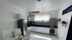 A modern kitchen with white cabinets, a stainless steel refrigerator, a gas stove, and a dining area with a glass table and white chairs. - Family Friendly~Chef Service- Book 8 to 14 Rooms (Sosua)