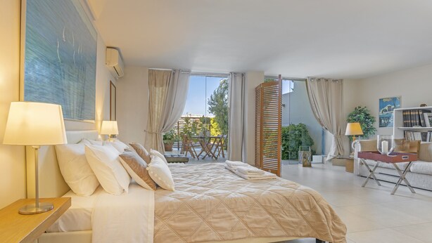 Une chambre d’hôtel moderne avec un grand lit, deux tables de chevet avec des lampes, un canapé, une petite table et une bibliothèque.