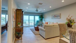 A spacious living room with a sofa, a coffee table, and a wicker chair. There is a balcony with a view of the ocean. -  Updated and Restored Beachfront Condo with Spectacular Views of the Gulf (Redington Shores)