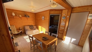 Un chalet confortable avec un intérieur en bois, une table à manger avec des chaises, un canapé, un lit et un petit coin cuisine.