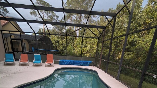 A swimming pool with a curved design, surrounded by a covered area with lounge chairs. -  The Wilson Wilds, A Peaceful 4BR Family Retreat, Private Pool 15 Mins to Disney (Davenport)