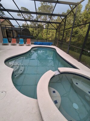 A swimming pool with a curved design, surrounded by a covered area with lounge chairs. -  The Wilson Wilds, A Peaceful 4BR Family Retreat, Private Pool 15 Mins to Disney (Davenport)