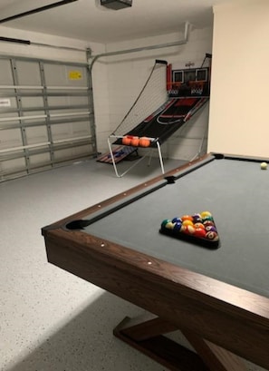 A pool table with balls, a rack, and a small table tennis table in a room with a garage door. - The Wilson Wilds (Davenport)