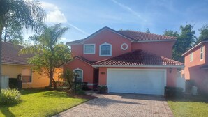 A two-story house with a red facade, a tiled roof, and a white garage door. -  The Wilson Wilds, A Peaceful 4BR Family Retreat, Private Pool 15 Mins to Disney (Davenport)