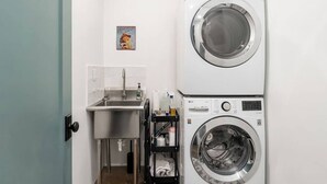 A laundry room with a stacked washer and dryer, a sink, and a small shelf with cleaning supplies.