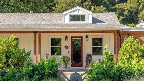A two-story house with a gabled roof, a front porch with a red door, and a sign reading "Le COOP".