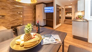 A modern hotel room with a dining area featuring a wooden table, a fruit bowl with bananas and pineapple, a bottle of wine, and magazines. - Tevini Boutique Suites - Apartment Water, balcony (Zell am See)