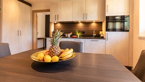 A modern kitchen with wooden cabinets, a stainless steel oven, and a fruit bowl on the dining table. - Tevini Boutique Suites - Apartment Earth, balcony (Zell am See)