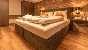 A neatly made bed with pillows and folded towels, a wooden headboard, and two bedside lamps. - Tevini Boutique Suites - Apartment Fire, balcony (Zell am See)