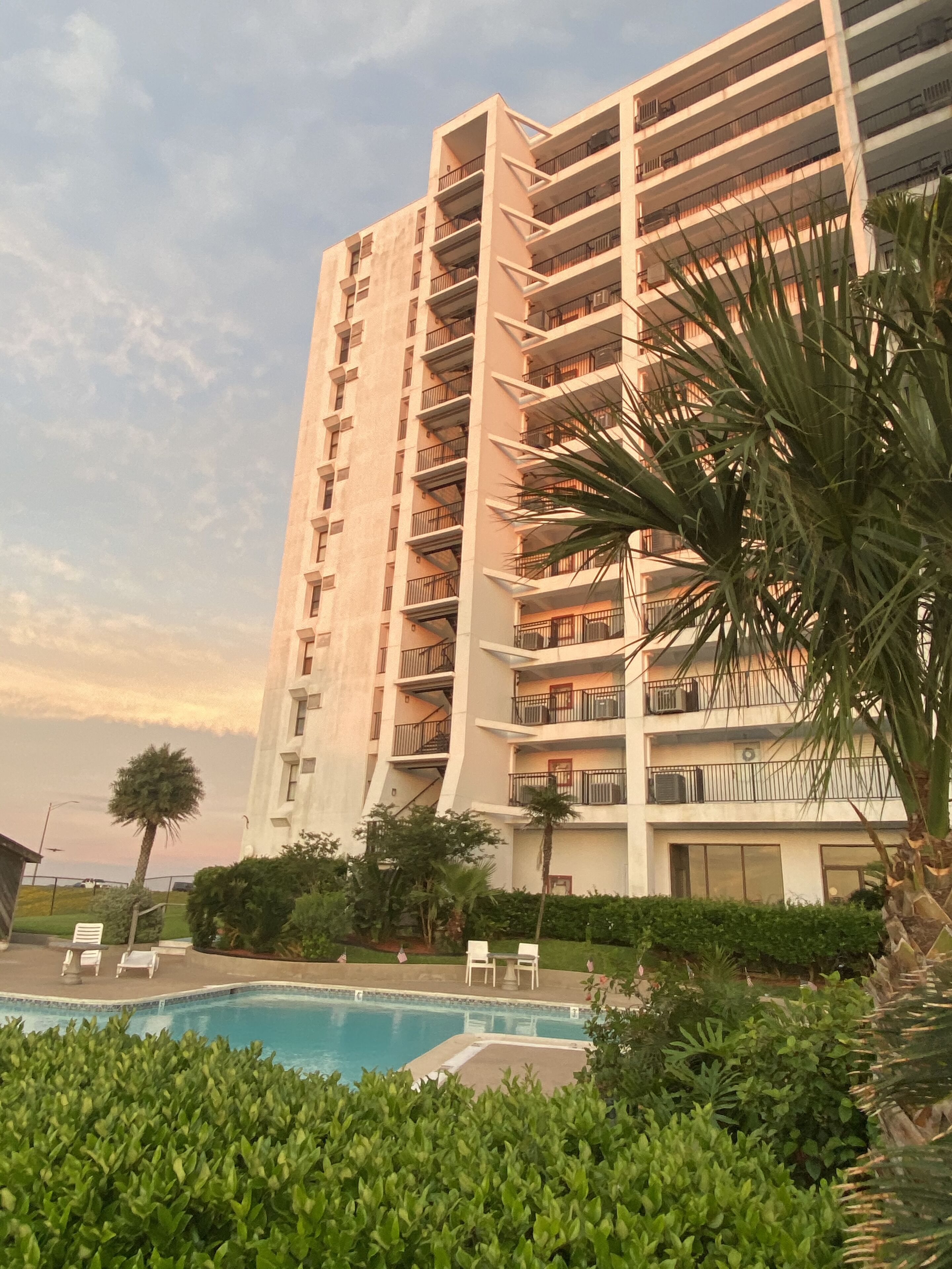 Un hotel de gran altura con varios balcones, una piscina y abundante vegetación.