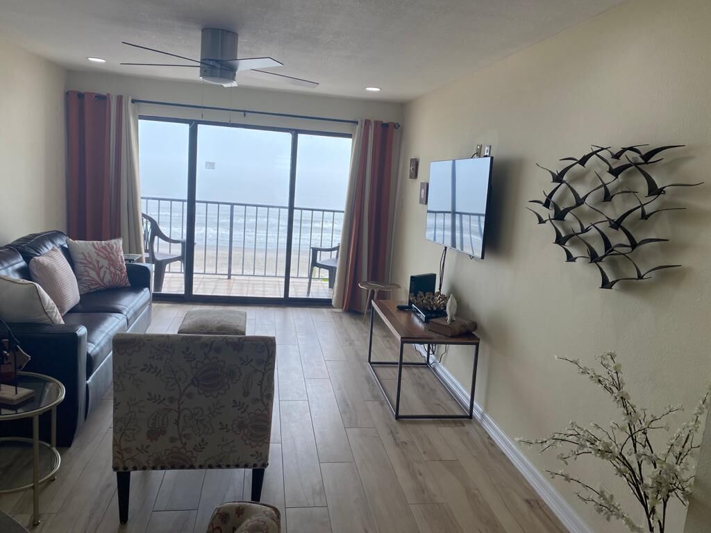 Un salon comprenant un canapé, un fauteuil et une table basse, un téléviseur fixé au mur, et un balcon avec vue sur l’océan.