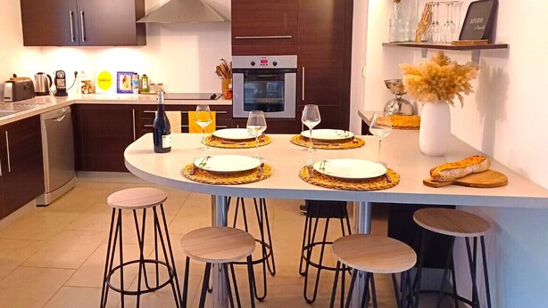 Una cocina moderna con armarios oscuros, horno integrado y una zona de comedor con taburetes y una isla central.