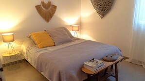 Un dormitorio ordenado con cama, lámparas de noche, una mesita con libros y adornos en la pared.