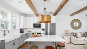 A modern kitchen with white cabinets, a central island with stools, stainless steel appliances, and a hanging copper light fixture.