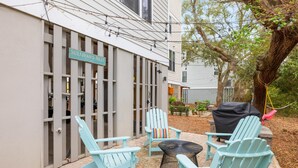 A patio area with light blue Adirondack chairs, a small round table, and a barbecue grill.