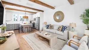 A modern kitchen with white cabinets, a central island, and wooden beams on the ceiling.