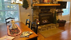 Una sala de estar acogedora con chimenea de piedra, una mesa de comedor con un ángel decorativo y un televisor.