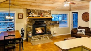 Una sala de estar acogedora con chimenea de piedra, techo de madera y televisor montado en la pared.