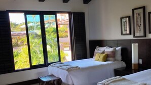 Ein modernes Hotelzimmer mit zwei Betten, einem Deckenventilator, großen Fenstern und Blick auf Grünflächen.