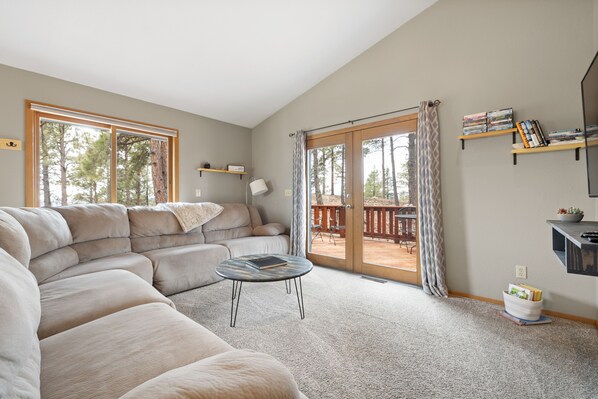A spacious living room with a large sectional sofa, a round coffee table, and a sliding glass door leading to an outdoor deck.