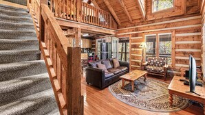 Ein Blockhaus-Interieur mit Treppe, einem Wohnzimmer, einer Couch, einem Couchtisch und einem Fernseher.