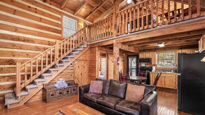 Ein Blockhaus-Interieur mit Treppe, Ledersofa, Esstisch und Küchenbereich.