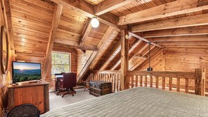 Ein Schlafzimmer im Dachgeschoss mit Holzboden, einem Bett, einem Schreibtisch, einem Stuhl und einem Fernseher.