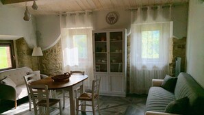 A rustic room with a wooden dining table, white chairs, a sofa, and a cabinet with glass doors. - Fonte Rosa farmhouse with pool (Fiastra)