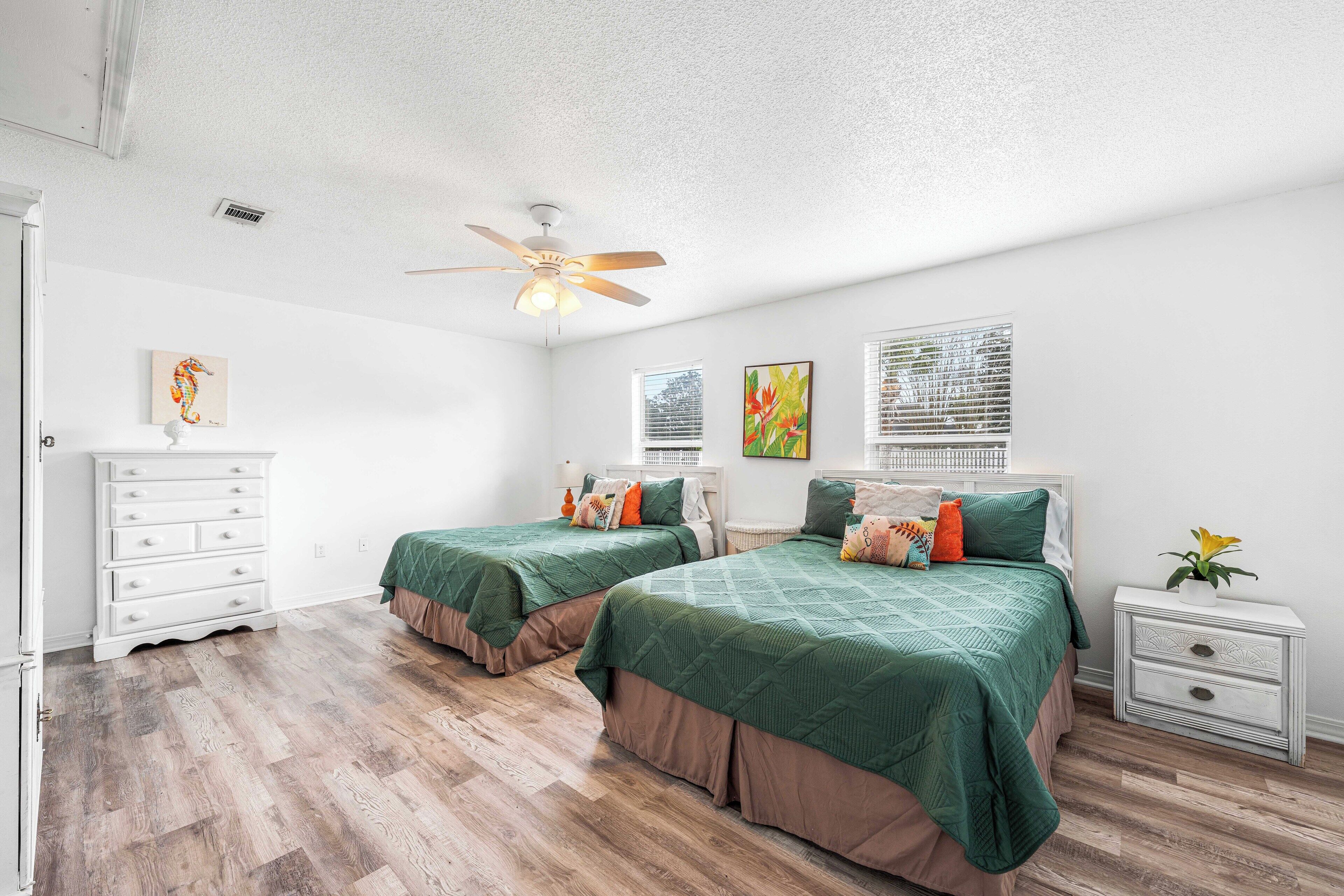 A bedroom with two beds, a ceiling fan, a dresser, and a nightstand with a plant.