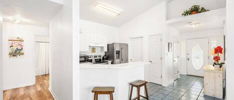 A spacious kitchen with white cabinets, a stainless steel refrigerator, and a central island with stools.
